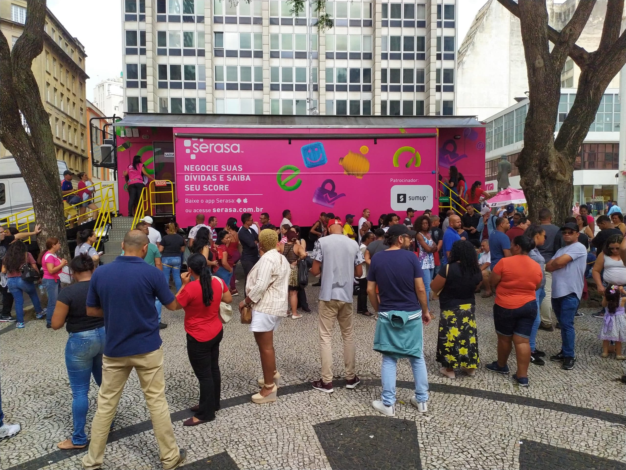 Imagem mostra um caminhão e uma fila de pessoas esperando atendimento