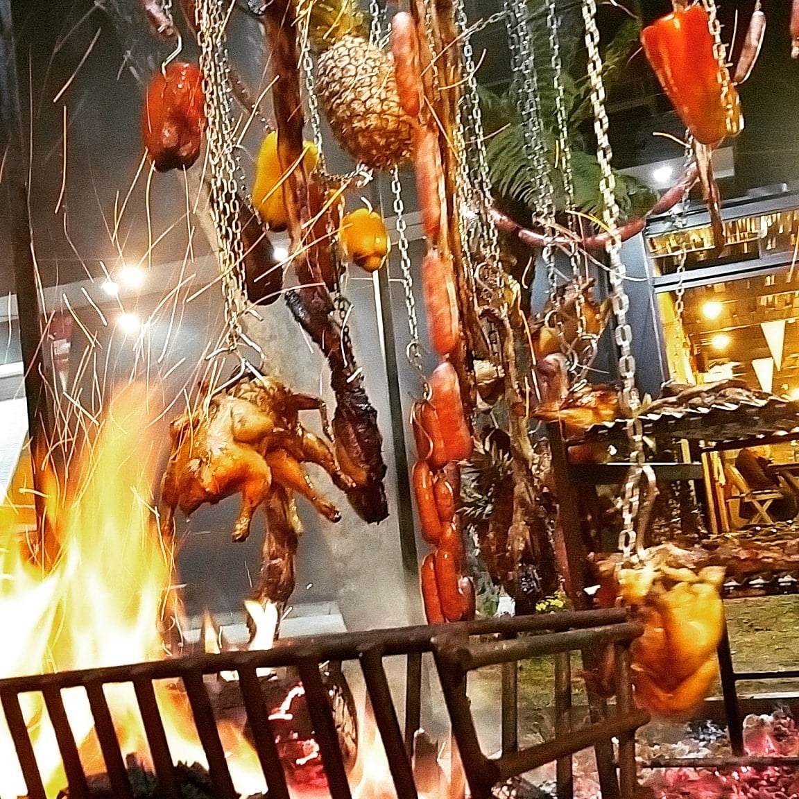 Foto mostra um varal com vários tipos de carne pendurados sobre um braseiro