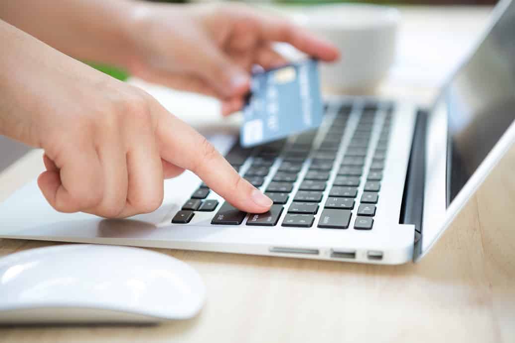 Foto mostra uma pessoa com o cartão de crédito e um teclado de computador